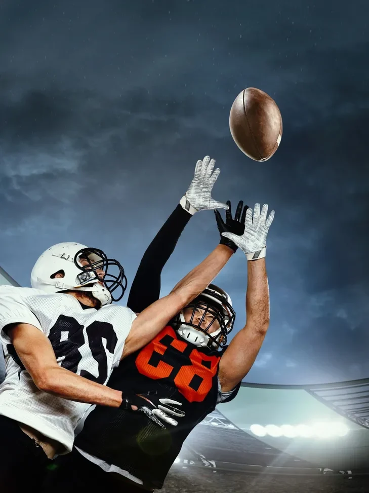 Two football players reaching for the ball mid-air during a game.