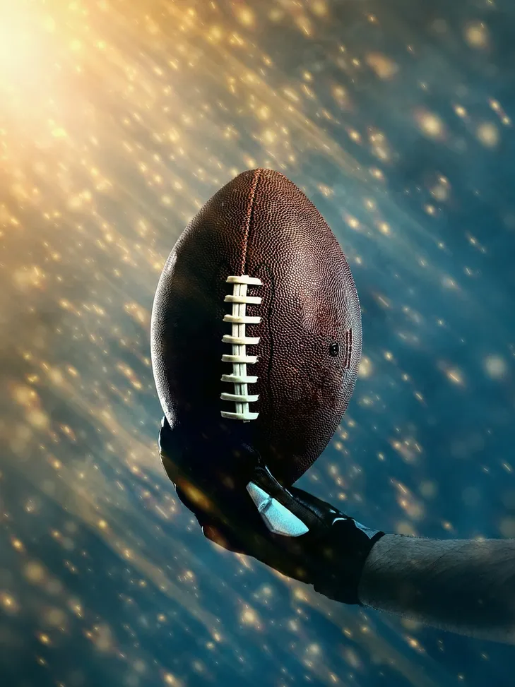 Hand holding a football against a glowing background.