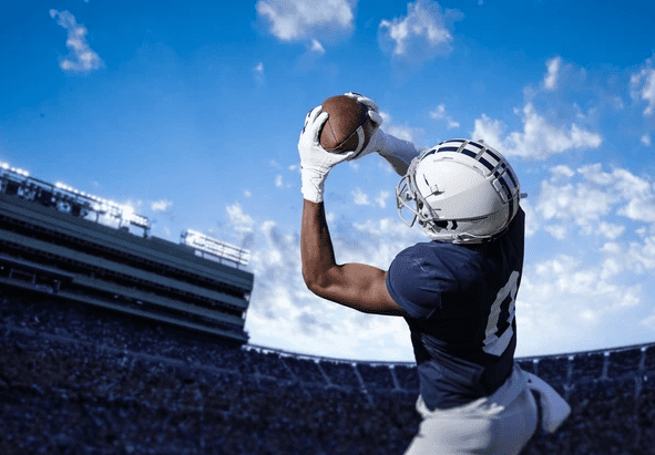 Football player catching a ball in a stadium under blue sky.